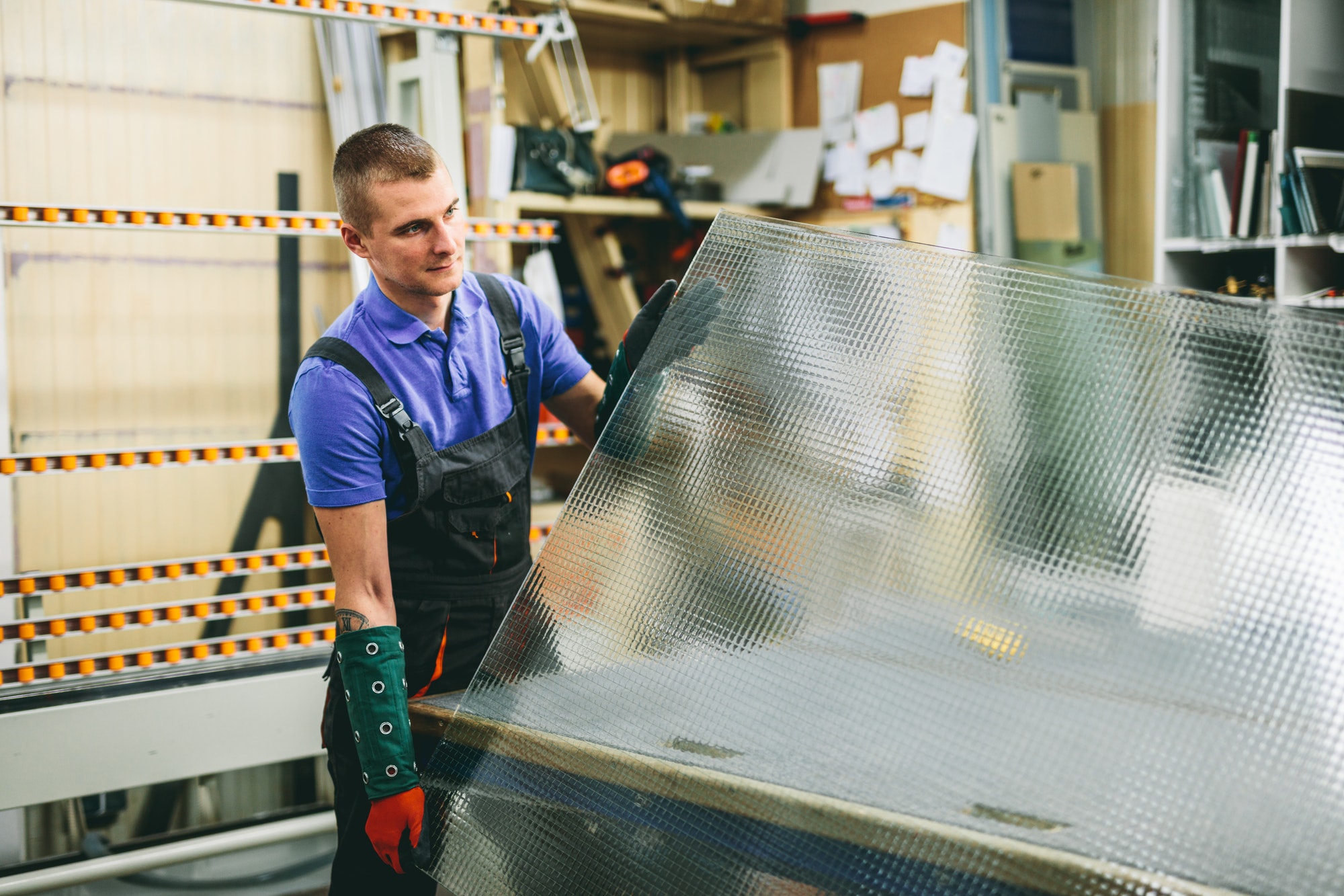 Glazier worker holding a big glass pane in workshop. Industry